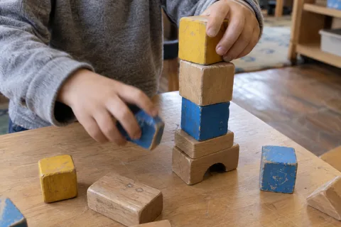 Illustrationsbild: Kinderhände stapeln Holzklötze auf einem Spieltisch