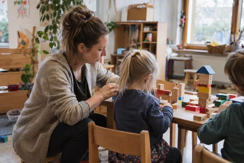 Illustrationsbild: Eine Erzieherin begleitet Kinder beim Bauen mit Holzklötzen